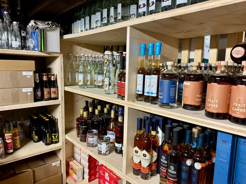 Rayons du magasin de Bourg-Saint-Pierre : eaux-de-vie du Valais, bières et bouteilles québécoises sur des étagères de bois